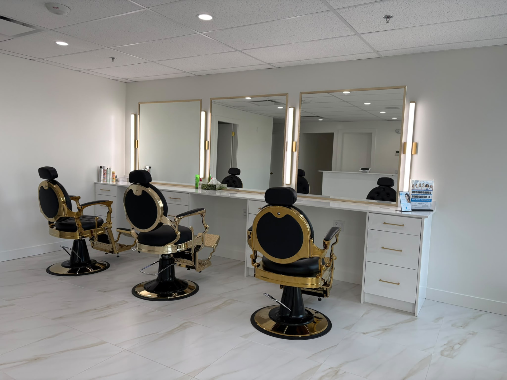 Three black and gold styling chairs beneath illuminated mirrors