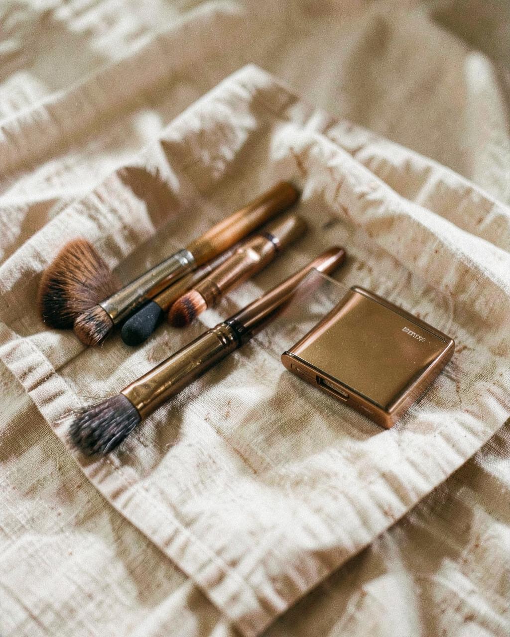 Bronze-toned makeup brushes on linen