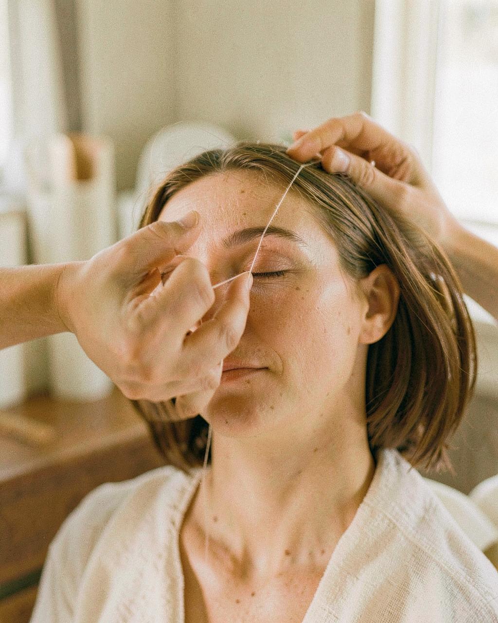 A beauty therapist threading a client's brow in a bright studio